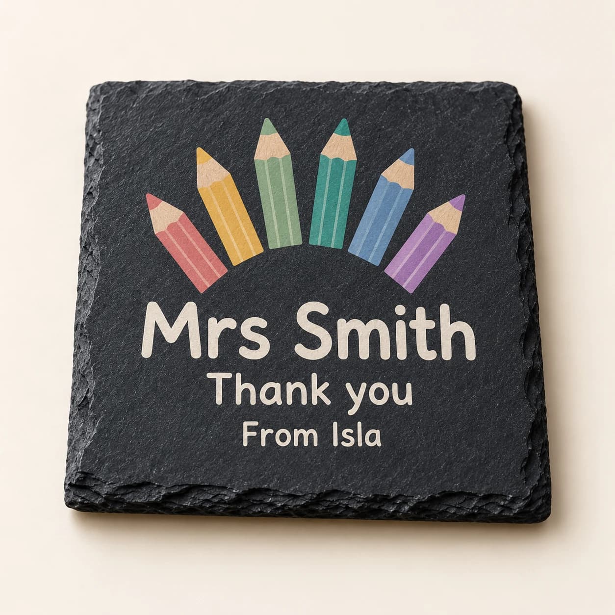 Digital product mockup of a slate teacher coaster with coloured pencils and a thank you message.