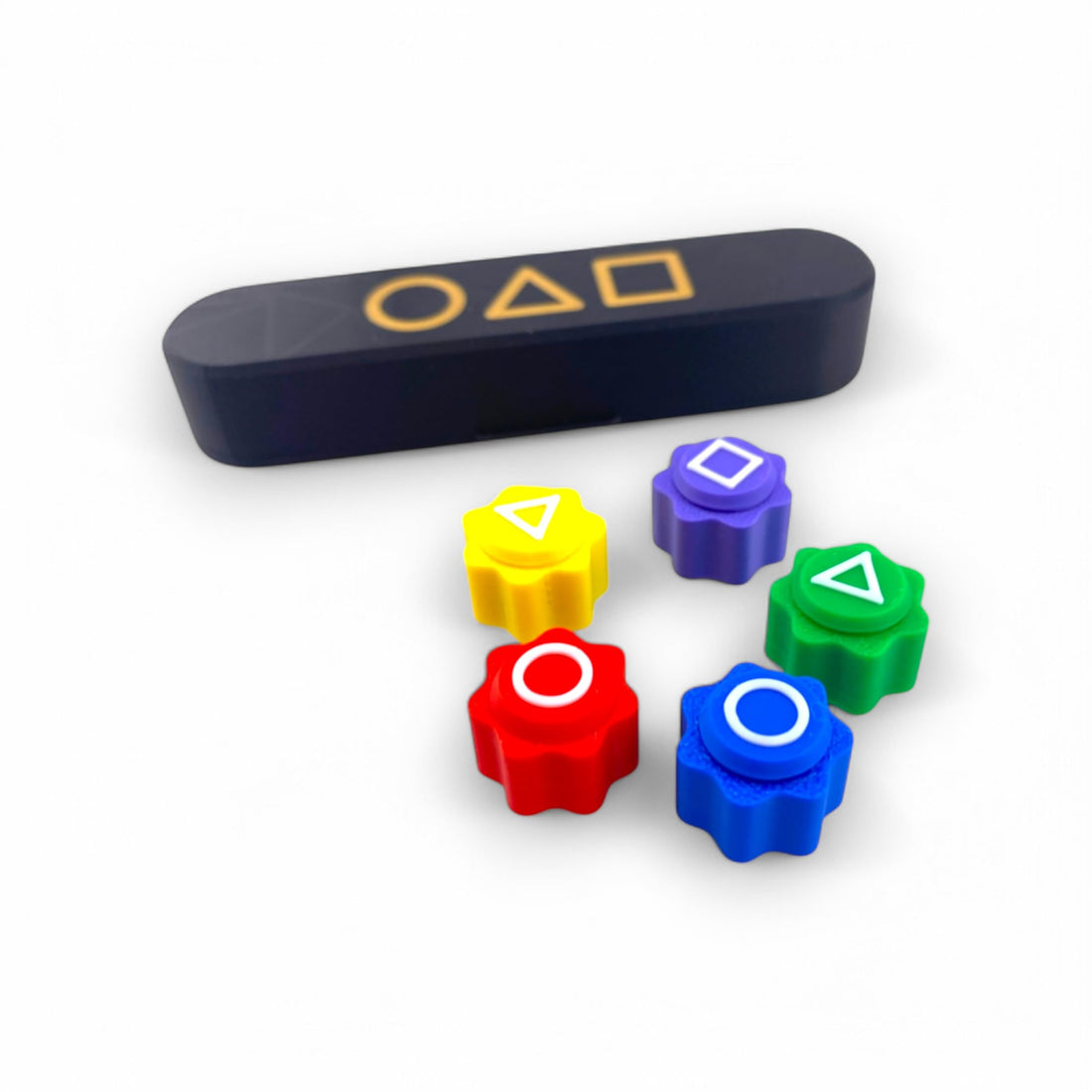 A set of colourful Gonggi game pieces in red, blue, green, yellow, and purple, each with distinct geometric symbols, alongside a black game case featuring matching shapes